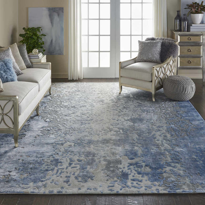 Living room with a Nourison Prismatic Denim rug, sofa, chair, and natural light. The rug has a modern, abstract design.