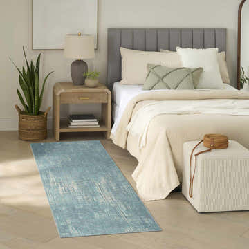 Bedroom scene with a Nourison Botanical Green rug, wood floors, neutral bedding, and a snake plant.