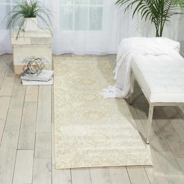 Light-filled room with Nourison Tranquility Ivory Bohemian rug, white bench, wood floors, and plants.
