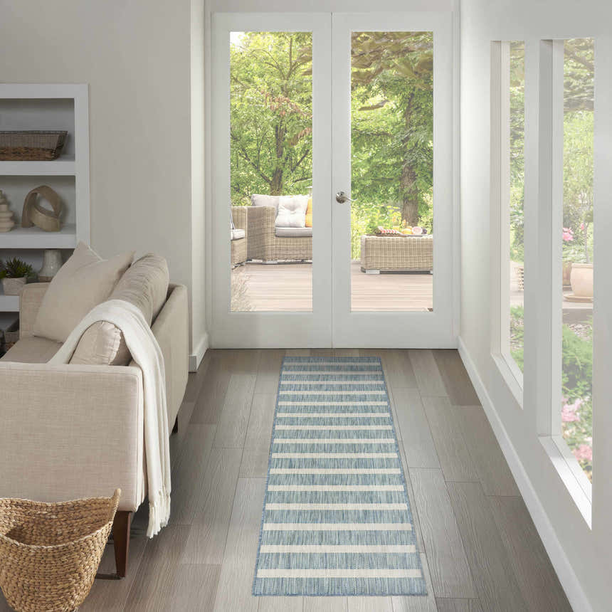 Hallway scene with a Nourison Positano Aqua Ivory rug, light wood floors, neutral sofa, and outdoor patio view.