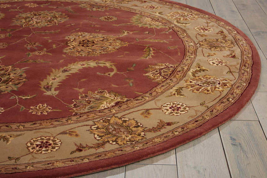 Close-up of a round Nourison 2000 Rose Persian rug. Features a pink floral pattern and a tan border on a wood floor.