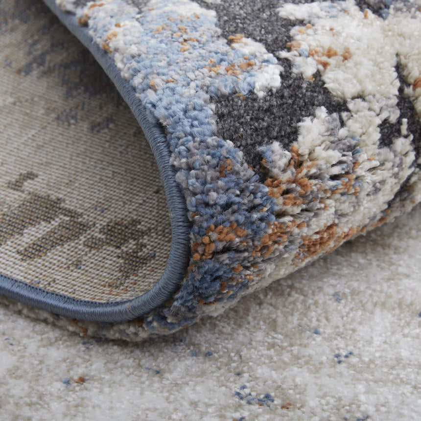 Close-up of Feizy Gilmore Ivory/Blue/Taupe Rug showing distressed pattern, soft texture, and blue binding. Fold