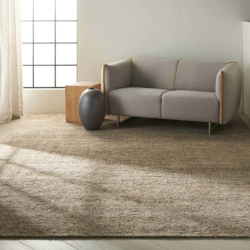 Minimalist living room with Calvin Klein Mesa Amber rug, gray sofa, wood block table, and natural light.