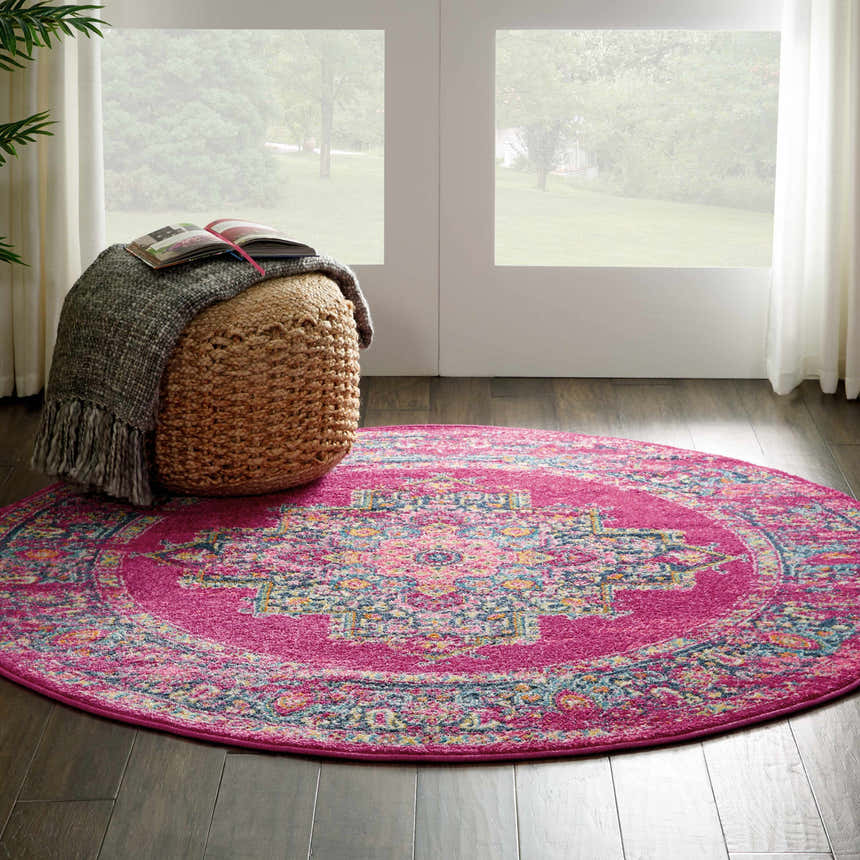 Bright entryway with a round Nourison Passion Fuchsia rug, pouf, book, wood floors, and natural light.
