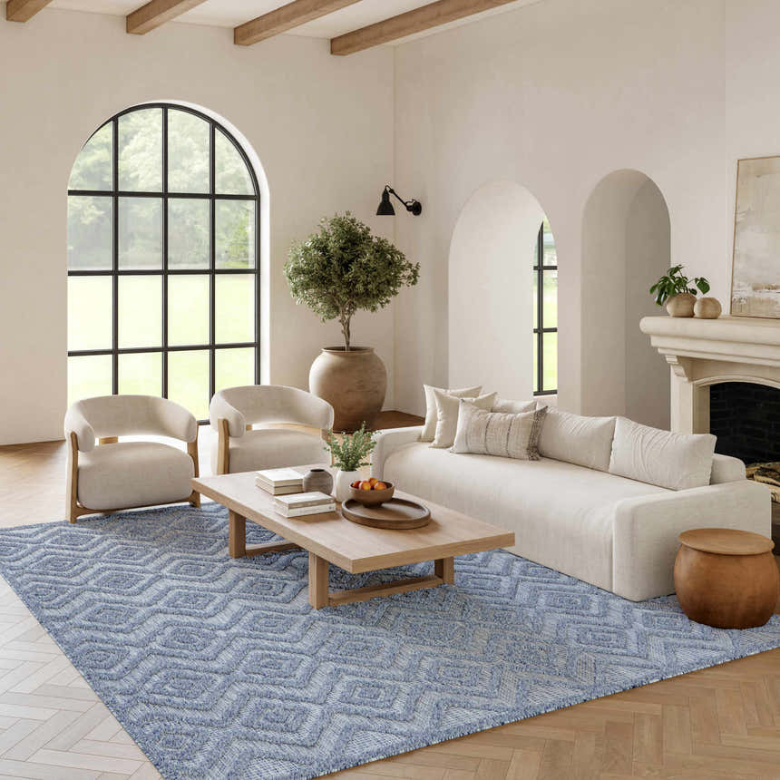 Living room scene with a denim blue Nourison Versatile rug, white sofa, wood accents, and arched windows for a modern aesthetic.