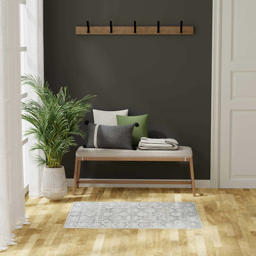 Entryway scene with a Nourison Dekor Grey Vintage Indoor Area Rug, bench, plant, and dark green accent wall.