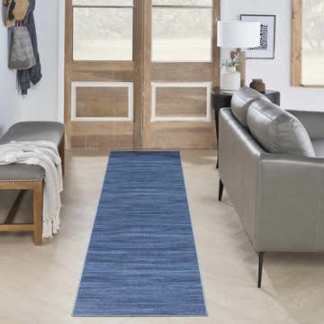 Entryway with Nourison s Blue Modern Indoor Washable Area Rug, gray sofa, wood door, and herringbone floors.