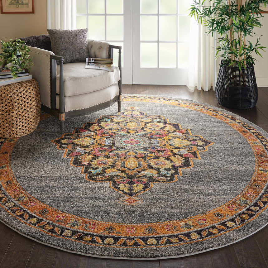 Living room scene with round Nourison Passionate Grey Bohemian rug, armchair, woven side table, and potted plant.