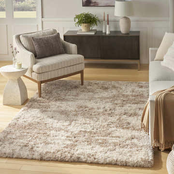 Living room scene with a Nourison Dreamy Shag ivory and dark beige rug, striped armchair, and light wood floors.