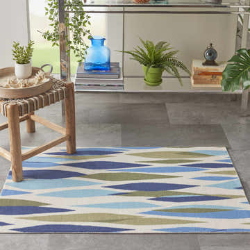 Entryway scene with Waverly Sun N' Shade Seaglass rug, blue and green geometric pattern, styled with a console table and stool.