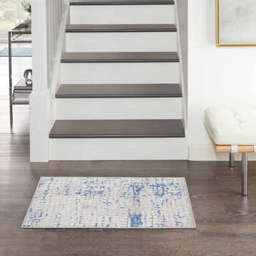 Entryway with a Nourison Whimsicle Grey Blue rug, white stairs, and a modern white bench on dark wood floors.