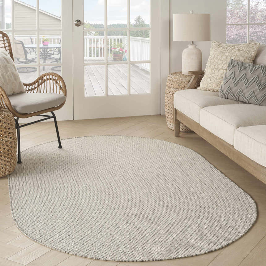 Living room scene with oval Nourison Courtyard Ivory Silver rug, light wood floors, sofa, and wicker chair.