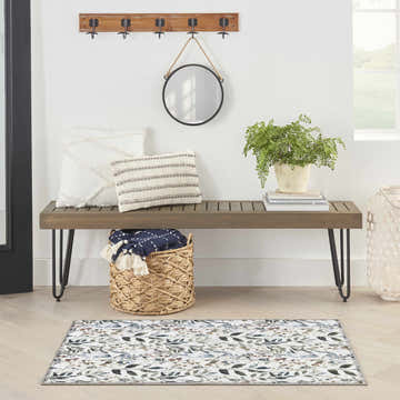 Entryway scene with Nourison Ivory Multicolor Contemporary Indoor Washable Area Rug, wood bench, mirror, and plant.