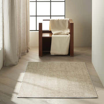 Minimalist room featuring a Calvin Klein Etched Ivory Beige rug, wood floors, chair, and neutral curtains.