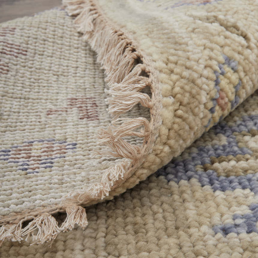 Close-up of the hand-knotted Feizy Fillmore rug. Tan wool with blue and brown floral pattern and fringe detail. Fold