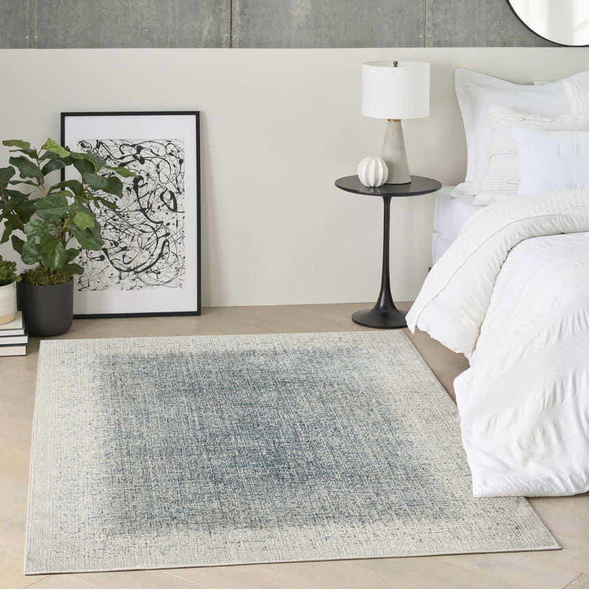 Modern bedroom scene with DKNY Grand Street Ivory Blue Area Rug, white bedding, side table, and abstract art.
