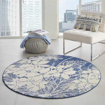 Modern living room with round Nourison Tranquil Beige Navy Floral rug, chair, and ottoman near a bright window.
