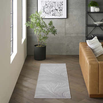 Modern living room with a tan leather sofa and DKNY Central Park West Grey runner rug on hardwood floors.