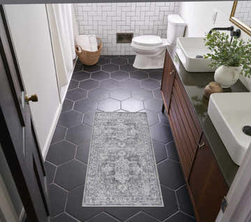 Bathroom scene with Nourison New Concept Ivory Grey Vintage Rug on black hexagon tile floor. Double sink vanity, white subway tile.