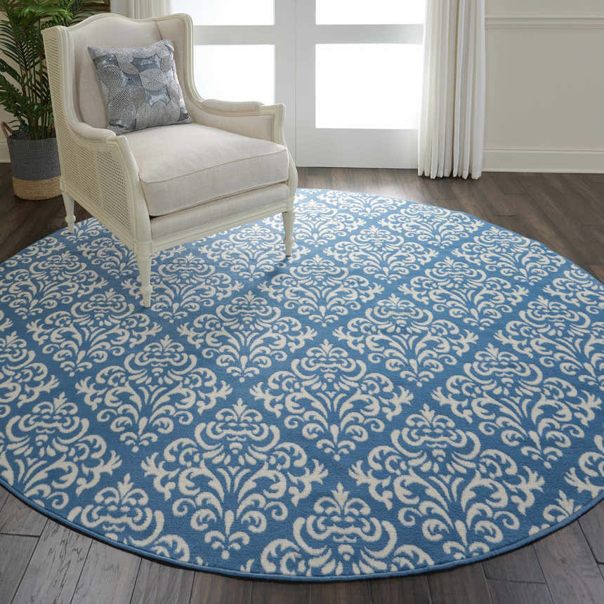 Living room scene with round Nourison Grafix Blue Vintage rug, white chair, dark wood floor, and natural light.