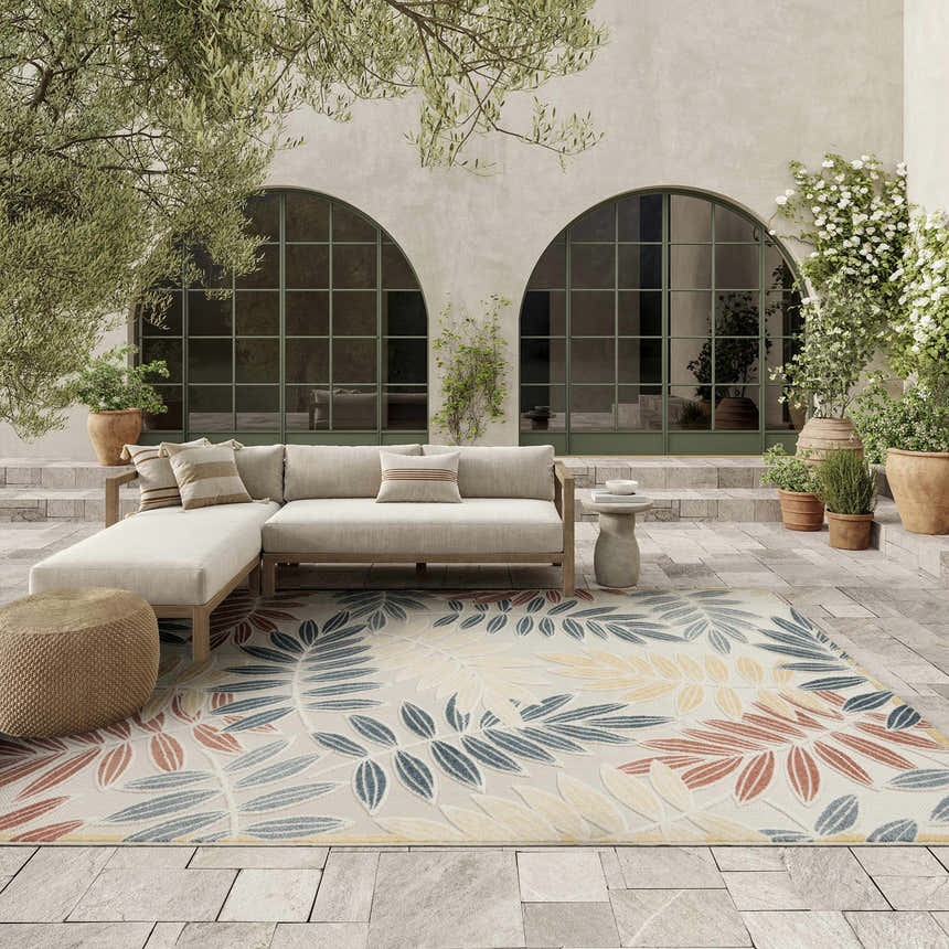 Outdoor patio scene with a Nourison Aloha Ivory Blue rug, sofa, and potted plants.