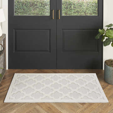 Entryway scene with Nourison Easy Care Ivory White rug, black double doors, wood floors, and potted plant.