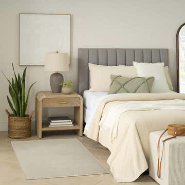 Serene bedroom scene with Nourison Charm Silver Ivory rug, wood nightstand, gray headboard, and neutral bedding.
