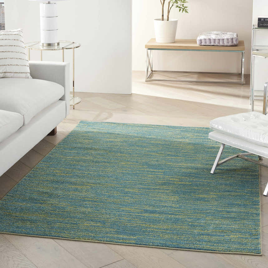 Living room scene with a Nourison Essentials Blue Green Outdoor Area Rug, white sofa, and light wood floors.
