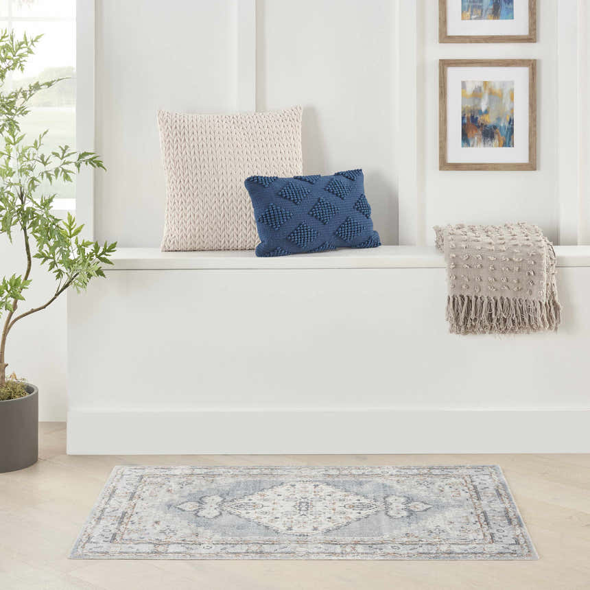 Entryway scene with a Nourison Astra Light Blue Vintage rug, pillows, throw, and potted plant.