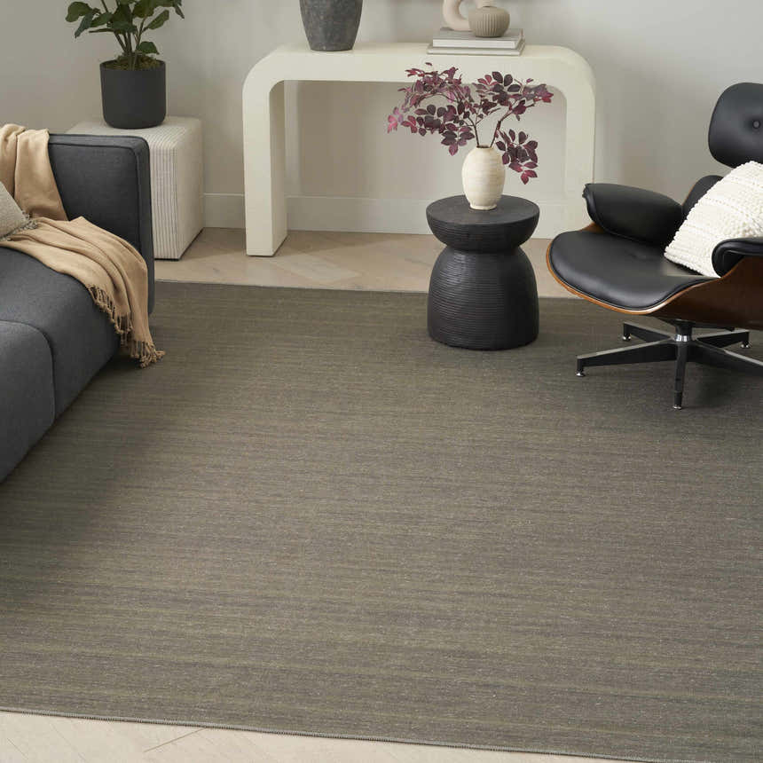 Modern living room with a Nourison Essentials Green rug, gray sofa, black chair, and white console table.