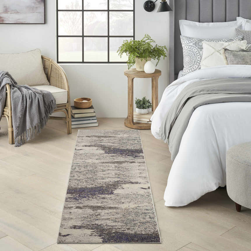 Bedroom scene with a Nourison Celestial Ivory Grey rug, light wood floors, rattan chair, and white bedding.
