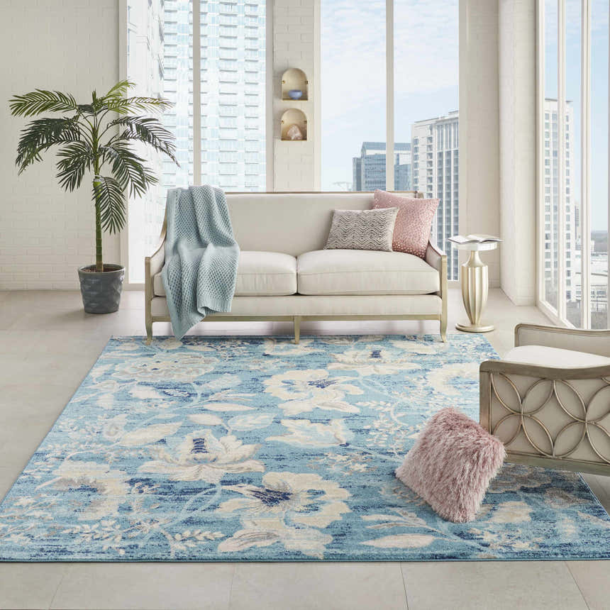 Living room scene with a Nourison Tranquil Turquoise Vintage rug, cream sofa, and city view. Aqua and pink accents.