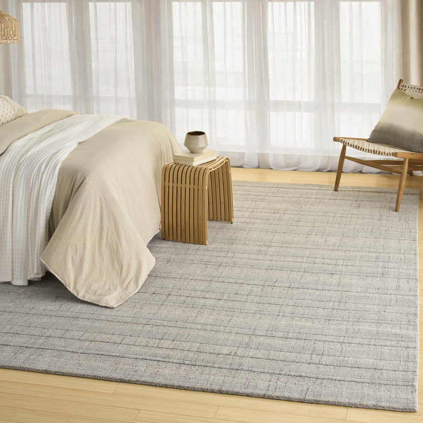 Neutral bedroom scene with DKNY Pure Multi Weave Grey rug, wood chair, side table, and light beige bedding.