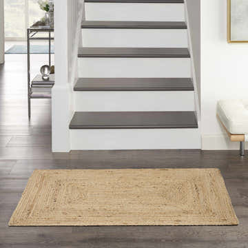 Entryway scene with a Nourison Natural Jute rug on dark wood floors by the stairs. Farmhouse style.