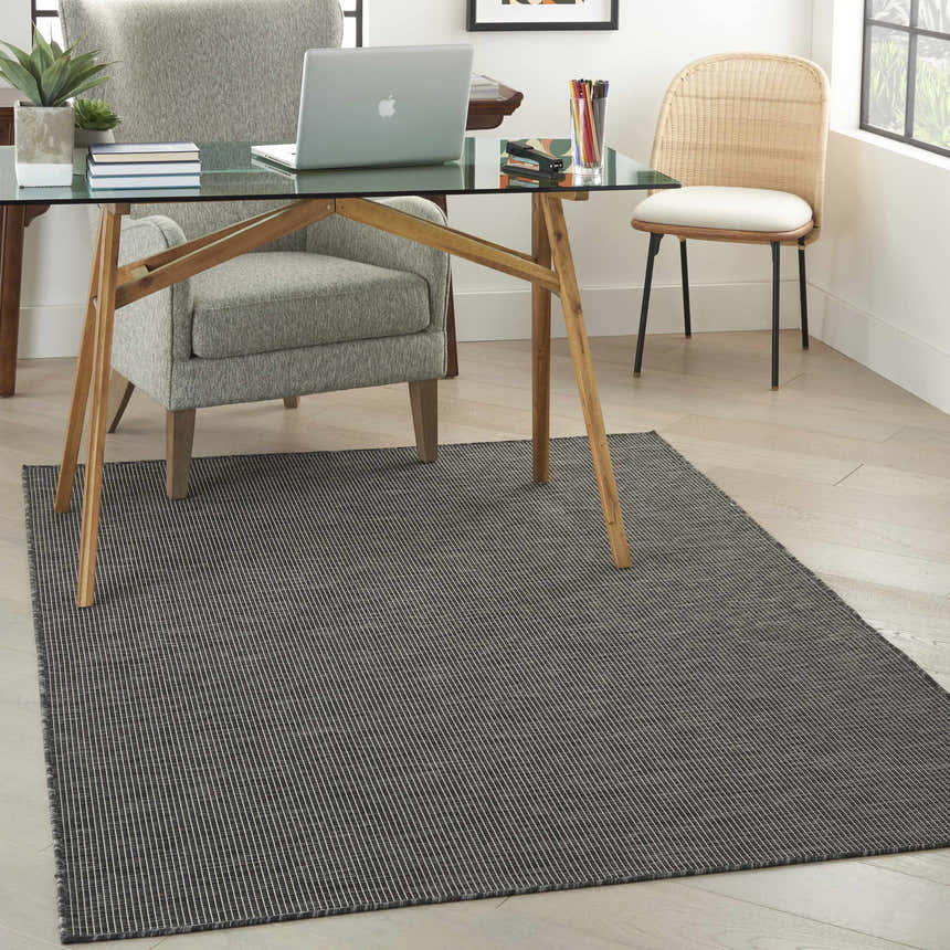 Home office with glass desk, gray chair, and Nourison Positano Charcoal rug. Modern, neutral tones.