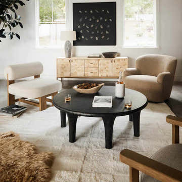 Living room scene with beige Four Hands Lalo Lambskin Rug, black coffee table, and neutral-toned furniture. Roomscene-Custom