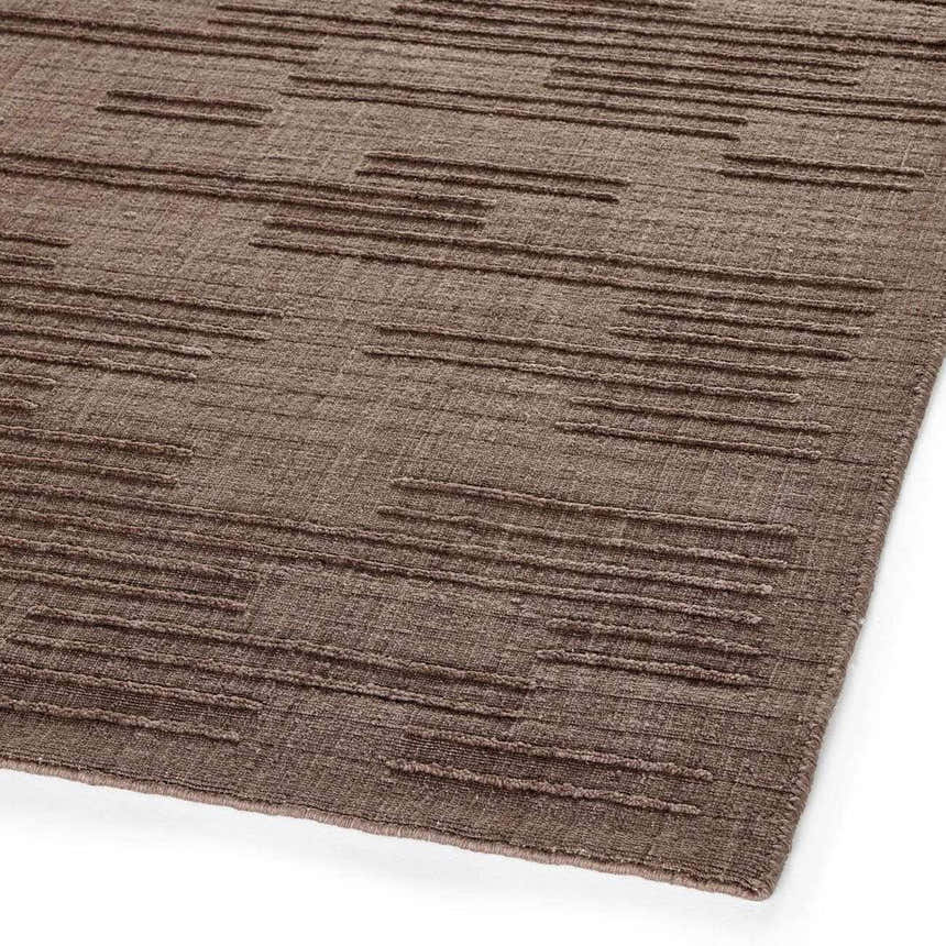 Close-up of the Four Hands Geist Rug - Akara Taupe. Taupe wool rug with a subtle, raised striped pattern. Hand-loomed texture. Corner