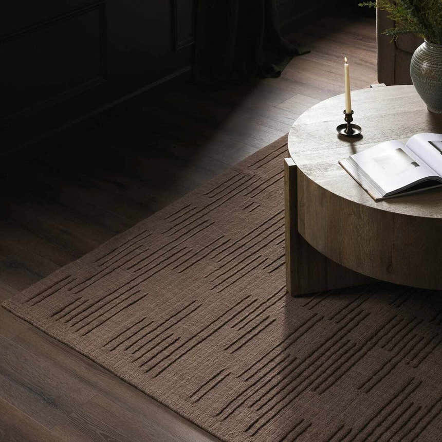 Living room scene with taupe Four Hands Geist Rug, wood floors, and round coffee table with book. Styleshot