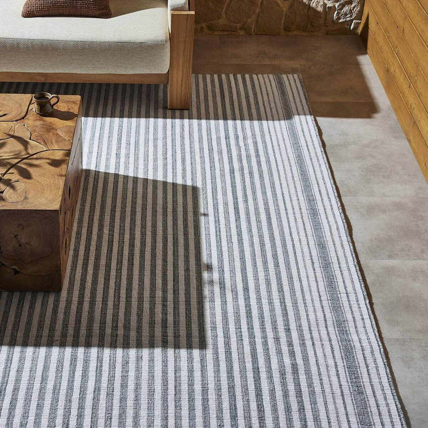 Four Hands Selena Outdoor Rug - Blue Stripe in a patio setting with wood furniture and stone wall. Styleshot