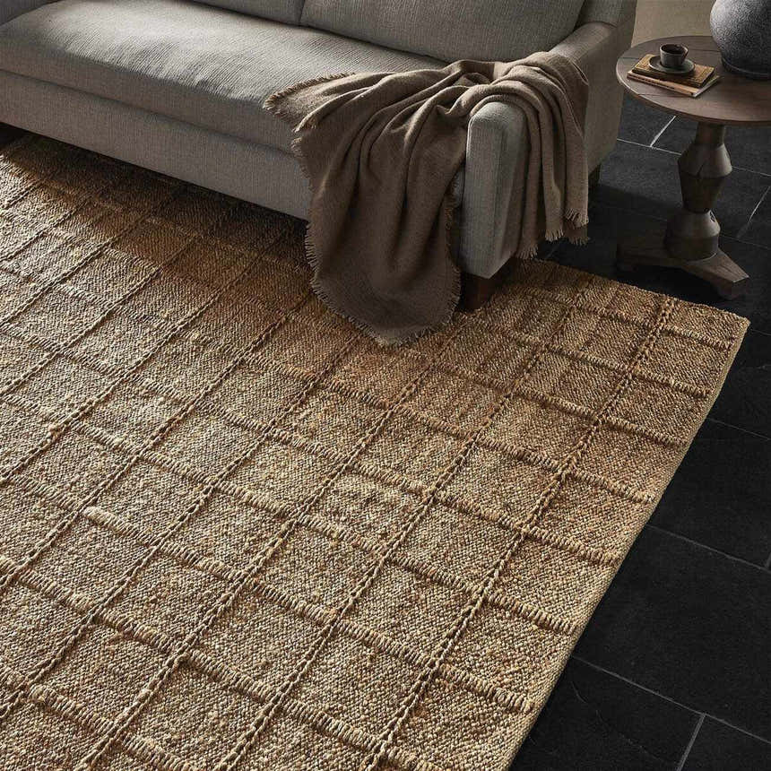 Living room scene with a Four Hands Grid Jute Rug, natural sofa, throw blanket, and dark stone tile flooring. Styleshot