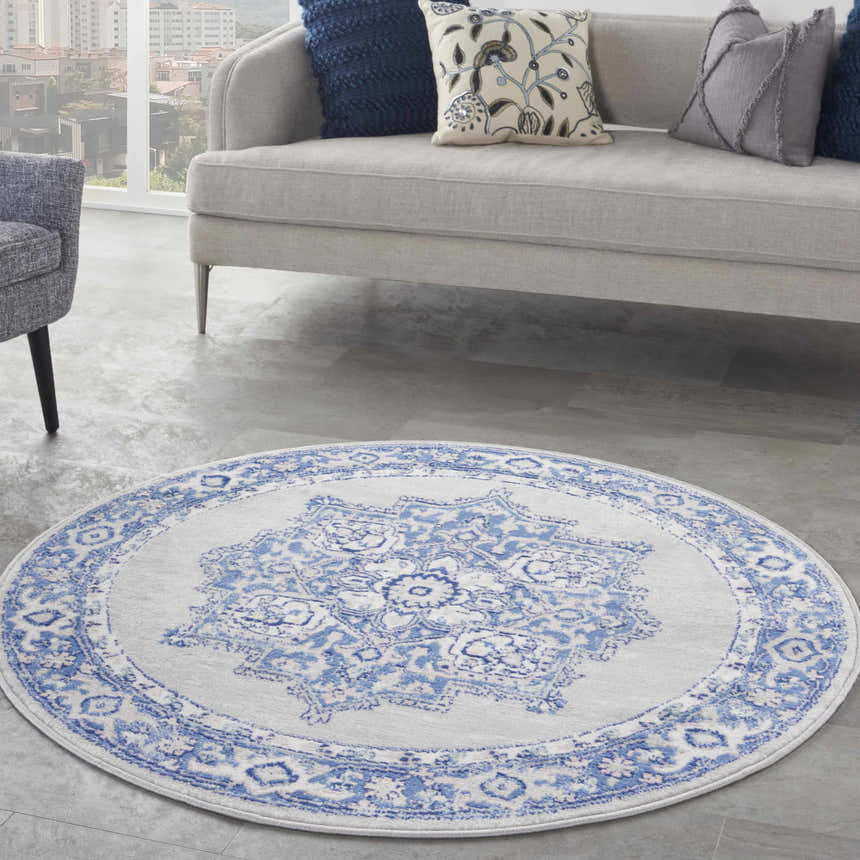 Living room scene with a round Nourison Whimsicle rug in grey and blue. Sofa, chair, and pillows complete the farmhouse style.