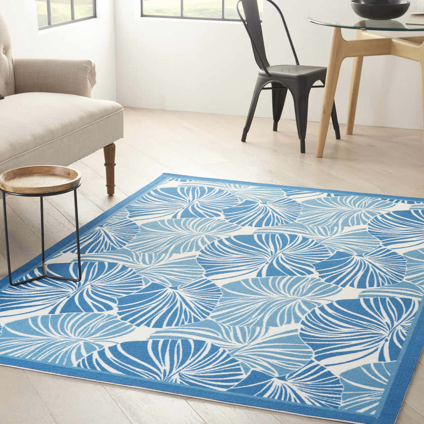 Living room scene with Waverly Sun N' Shade Blue Tropical Area Rug, beige armchair, wood table, and dining set.