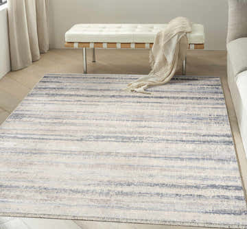 Modern living room with a light blue Calvin Klein CK089 Drift rug, white bench, and neutral decor.