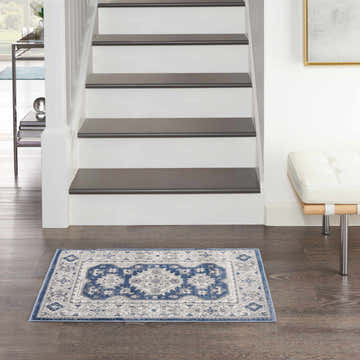 Entryway with a Nicole Curtis Series 4 Grey Navy Vintage rug, stairs, and white bench.