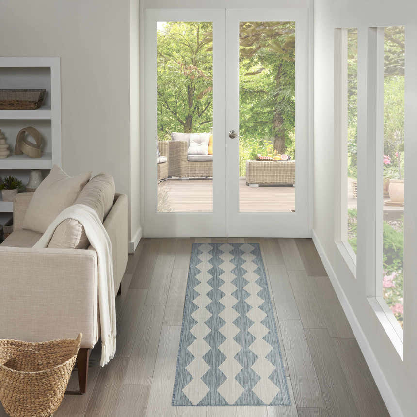 Light-filled hallway with a Nourison Positano Aqua Modern Area Rug runner, neutral sofa, and view to an outdoor patio.