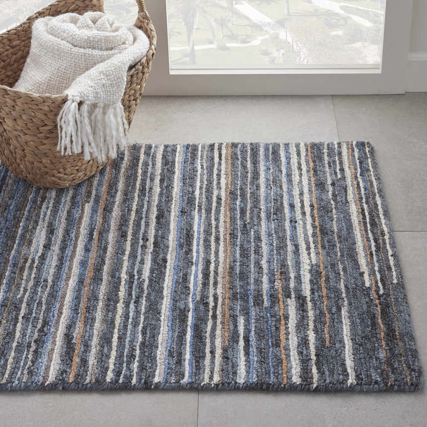 Modern entryway with blue striped Nourison Plateau Blue rug, woven basket, and rolled throw blanket.