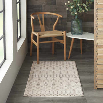 Modern room scene with a beige and gray Nourison Palermo bohemian area rug, wood chair, and white accent table.