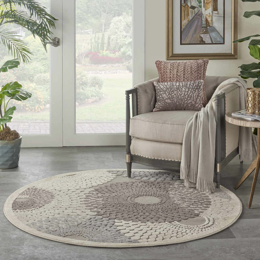 Sunlit room with a round Nourison Graphic Illusions grey rug, armchair, and plants. Mid-century modern style.
