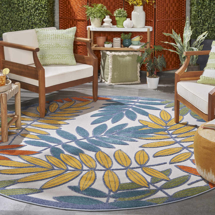 Tropical patio scene with a round Nourison Aloha Ivory Multicolor area rug, wood chairs, and green accents.