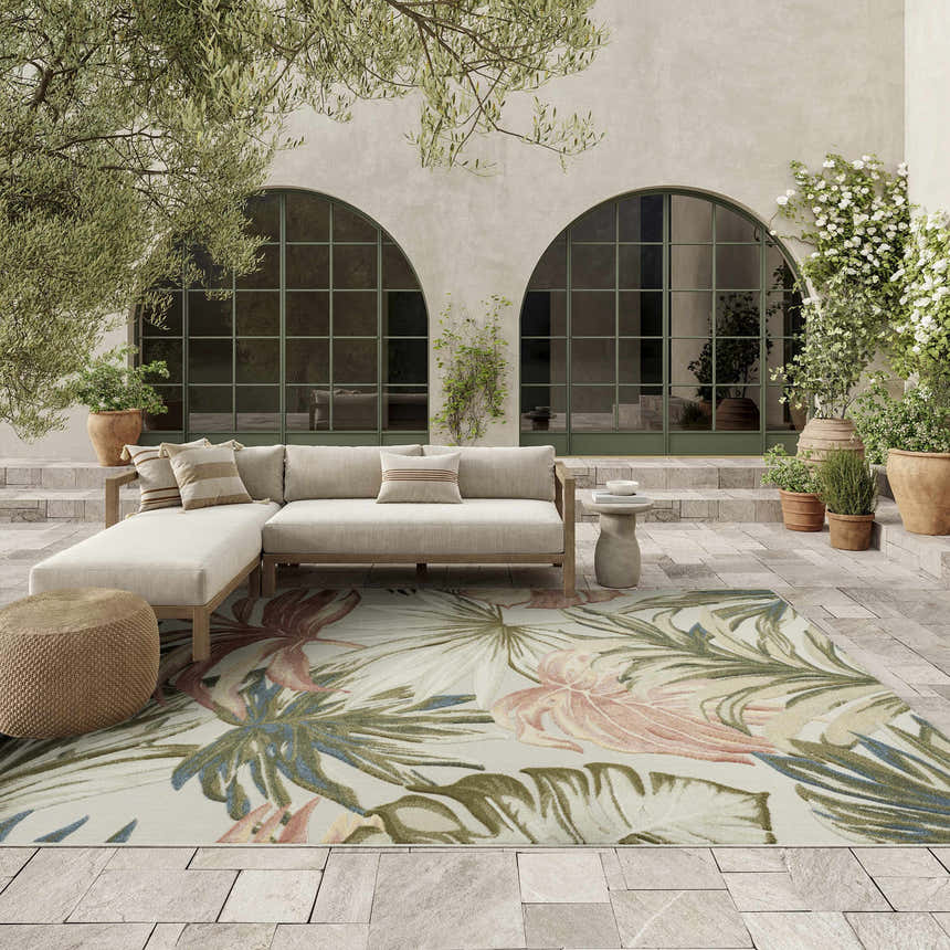 Outdoor patio with sectional sofa and Nourison Aloha Ivory Green Area Rug featuring a tropical floral pattern.